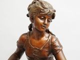 bronze statue of a woman sitting on a stool with her legs crossed