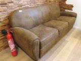 a brown leather couch with a fire extinguisher next to it
