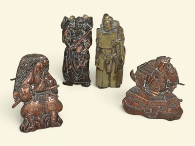 trois figurines en bronze représentant des personnes assises sur une surface blanche