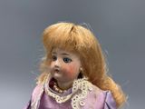 a doll that is wearing a purple dress and a pearl necklace