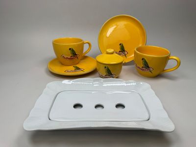 a white plate with a yellow cup and saucer and a yellow plate with a bird on it