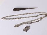 une chaîne en argent et un couteau posés sur une surface blanche