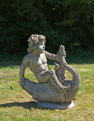 une statue représentant une sirène assise sur un rocher dans l'herbe