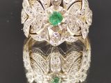 une photo d'une bague sertie d'un diamant et d'une émeraude, posée sur une surface réfléchissante