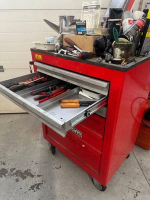 une boîte à outils rouge posée dans un garage, avec des outils dessus