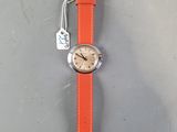 an orange strap on a watch on a gray surface with a tag