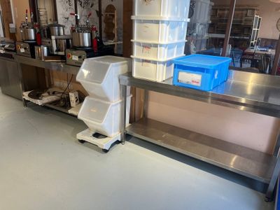 une grande cuisine avec un plan de travail en inox et une poubelle bleue posée par terre
