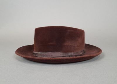 Le chapeau est marron et est orné d'une plume sur le dessus.