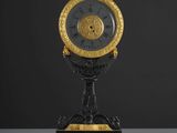 une horloge ancienne noire et dorée, avec des chiffres romains, posée sur un socle
