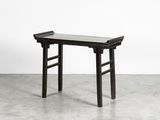 une table en bois noir avec un plateau en verre, posée sur un sol en ciment