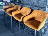Quatre tabourets de bar en velours orange sont alignés contre un mur en pierre