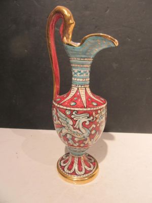 a red and blue vase with a gold handle on a white table