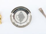 a silver bowl with a spoon and a gold object next to it
