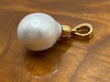 a white pearl on a gold plated pendant on a wooden table
