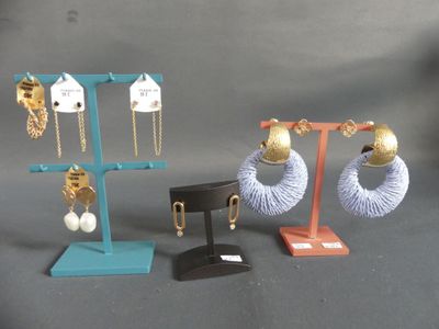 Trois paires de boucles d'oreilles sont présentées sur un présentoir, sur un fond gris.