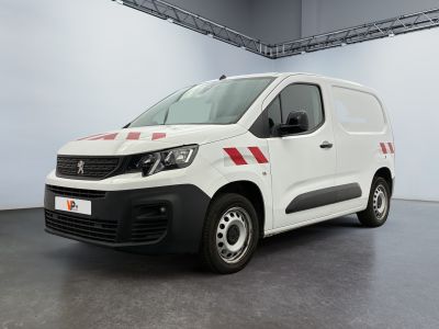 La camionnette blanche est garée à l'intérieur d'un bâtiment ; elle porte une bande rouge sur le côté.