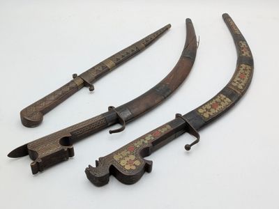 three antique chinese swords with wooden handles on a white surface