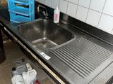 un évier au milieu d'une cuisine dont le plan de travail est encombré