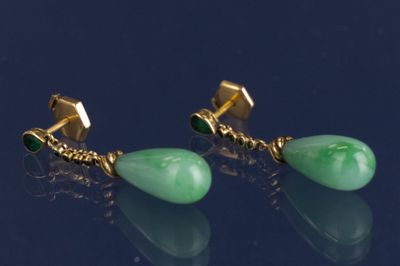 une paire de boucles d'oreilles en or et en jade vert sur un fond noir