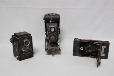 trois vieux appareils photo posés les uns à côté des autres sur une surface blanche