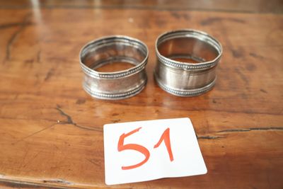 deux ronds de serviette en argent posés sur une table en bois portant le numéro 51