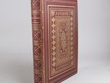 an old red book with gold trim sitting on top of a white surface