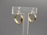 paire de boucles d'oreilles créoles dorées, présentées sur un support en acrylique transparent