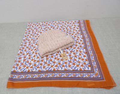 une couverture orange et blanche sur laquelle est posé un bonnet