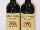 two bottles of red wine sitting on top of a white table