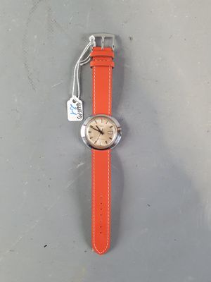 an orange strap on a watch on a gray surface with a tag