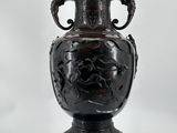 un grand vase noir posé à côté d'une pomme sur un fond blanc