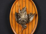 a bronze bird on a wooden plate on a wall
