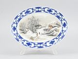 an oval blue and white plate with a painting of a winter scene on it