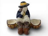 une figurine représentant un homme coiffé d'un chapeau et chaussé de bottes, assis sur un tonneau