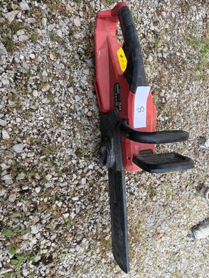 a red and black chainsaw on the ground next to a cat