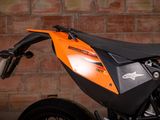 an orange and black motorcycle parked in front of a brick wall