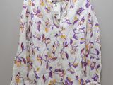 a white shirt with purple and yellow flowers is hanging on a hanger