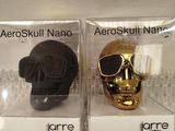 pair of black and gold skulls in clear boxes on lace tablecloth