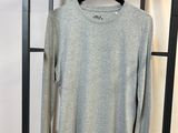un t-shirt gris à manches longues suspendu à un porte-vêtements dans une pièce