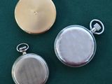two silver and gold pocket watches sitting on a green surface