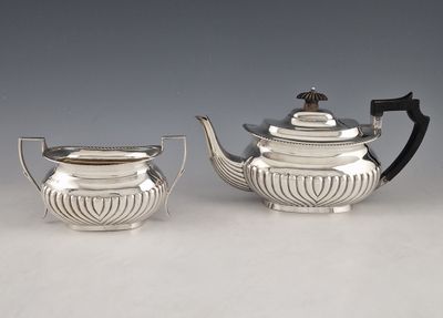 a pair of silver teapots and a sugar bowl on a table
