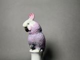 a figurine of a pink parrot sitting on a white cup