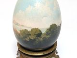 a blue and white egg on a stand with trees in the background