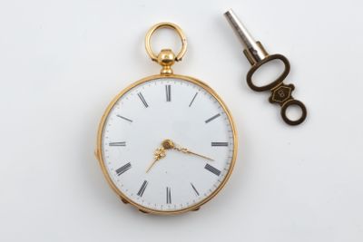 a gold pocket watch and a key on a white surface
