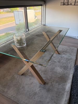 une table en verre avec des pieds en bois, sur laquelle se trouve un vase