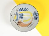 une assiette sur laquelle est représenté un oiseau, sur un fond jaune et blanc