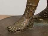 a bronze statue of a person with a foot on a table