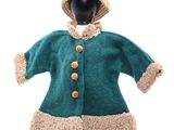une poupée vêtue d'un manteau vert et d'un chapeau, posée sur un mannequin noir