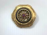 a close up of a gold and black broochle on a white surface