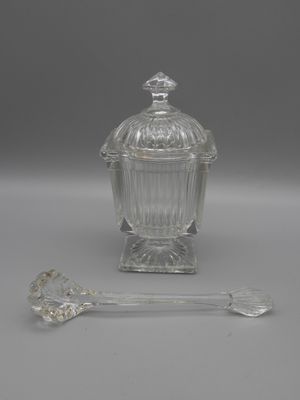 an antique glass jar with a spoon and spoon rest on a table